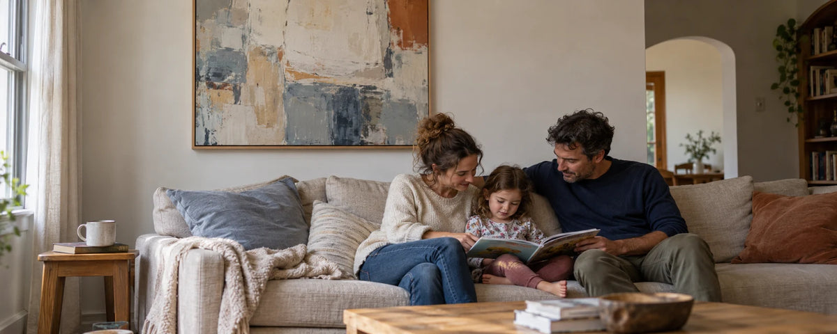 A family sharing a quiet reading moment in a naturally lit living room with abstract wall art.